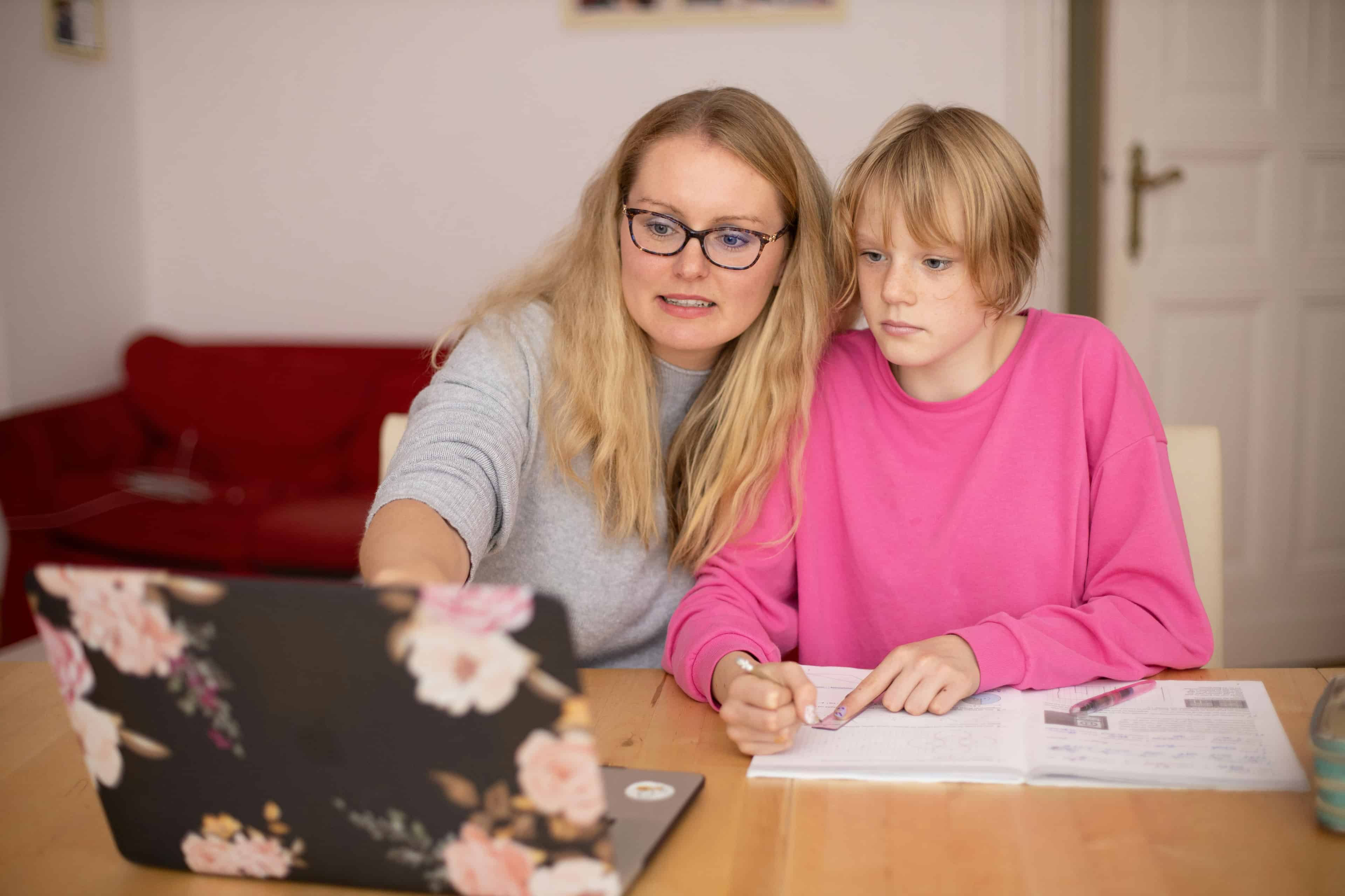 A mother helping her young daughter with schoolwork on a laptop at home, symbolizing parent involvement in education.
